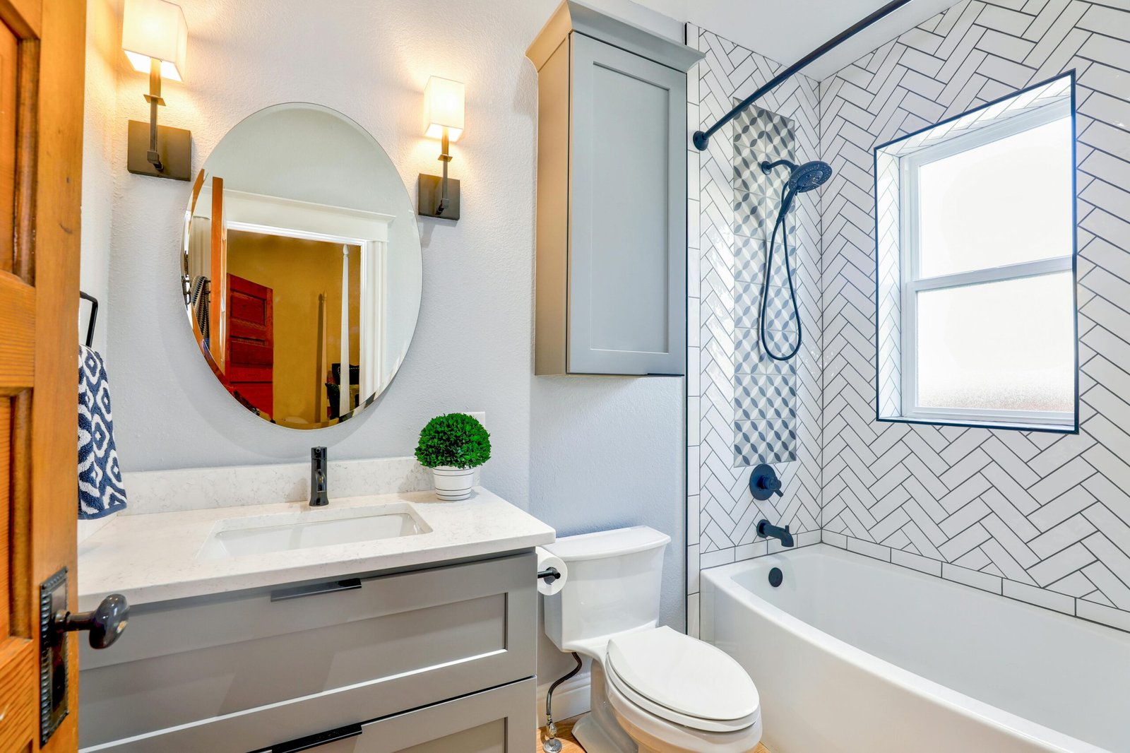 Our Services Elegant modern bathroom featuring chevron tiles, oval mirror, and sleek fixtures for a contemporary look.